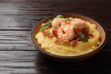 Photo of Fresh tasty shrimps, bacon, grits and basil in bowl on wooden table, closeup