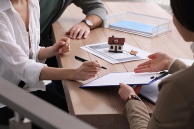 Young couple signing purchase contract in real estate agent's office, closeup. Mortgage concept