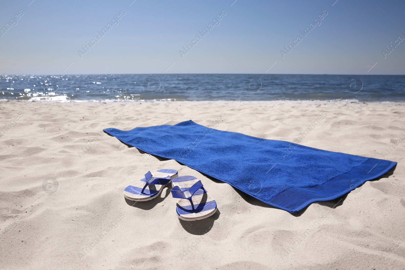 Photo of Flip flops and blue beach towel on sandy seashore