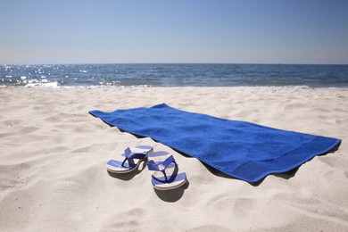 Photo of Flip flops and blue beach towel on sandy seashore