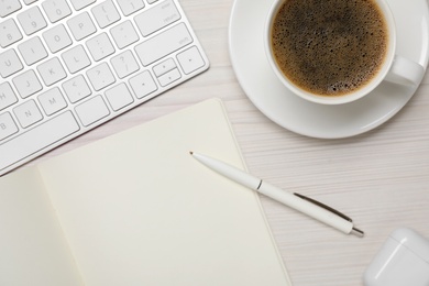 Photo of Notebook with pen near cup of coffee and computer keyboard on white wooden table, flat lay