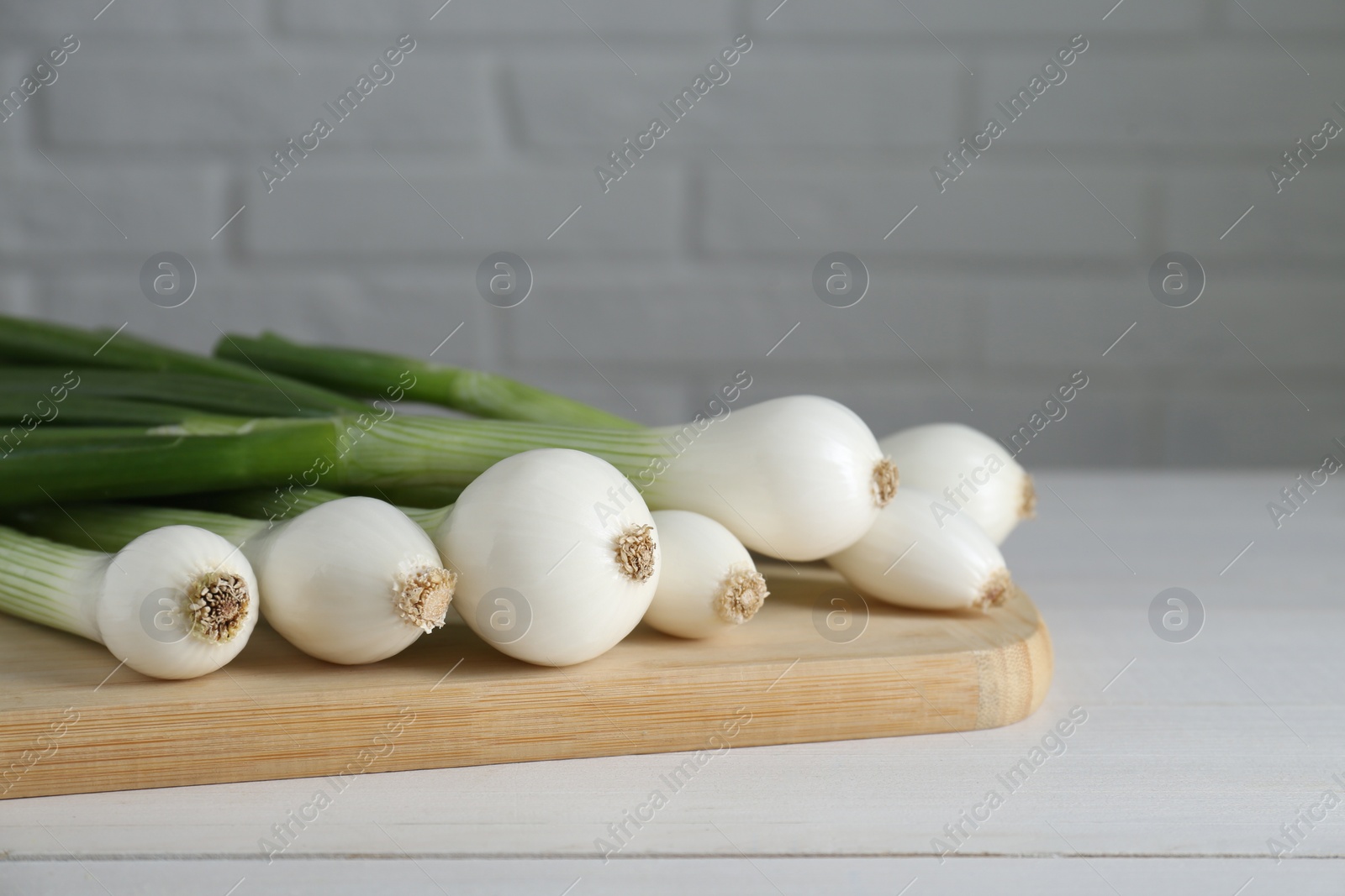 Photo of Fresh green spring onions on white wooden table, closeup. Space for text