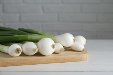 Photo of Fresh green spring onions on white wooden table, closeup. Space for text