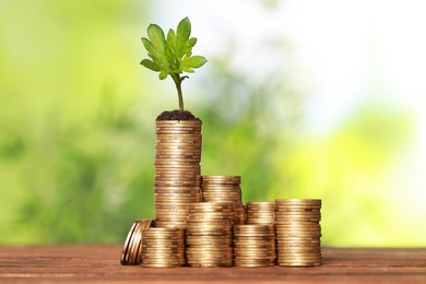 Photo of Stacked coins and green sprout on wooden table against blurred background. Investment concept