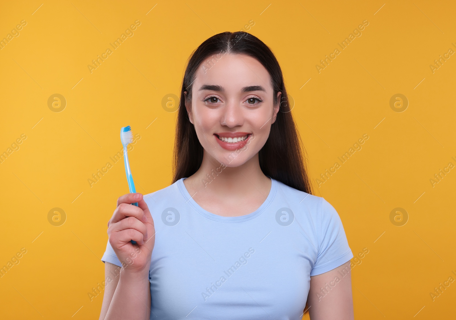 Photo of Happy young woman holding plastic toothbrush on yellow background