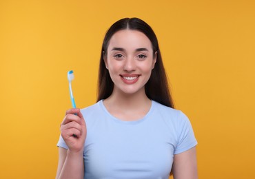 Happy young woman holding plastic toothbrush on yellow background