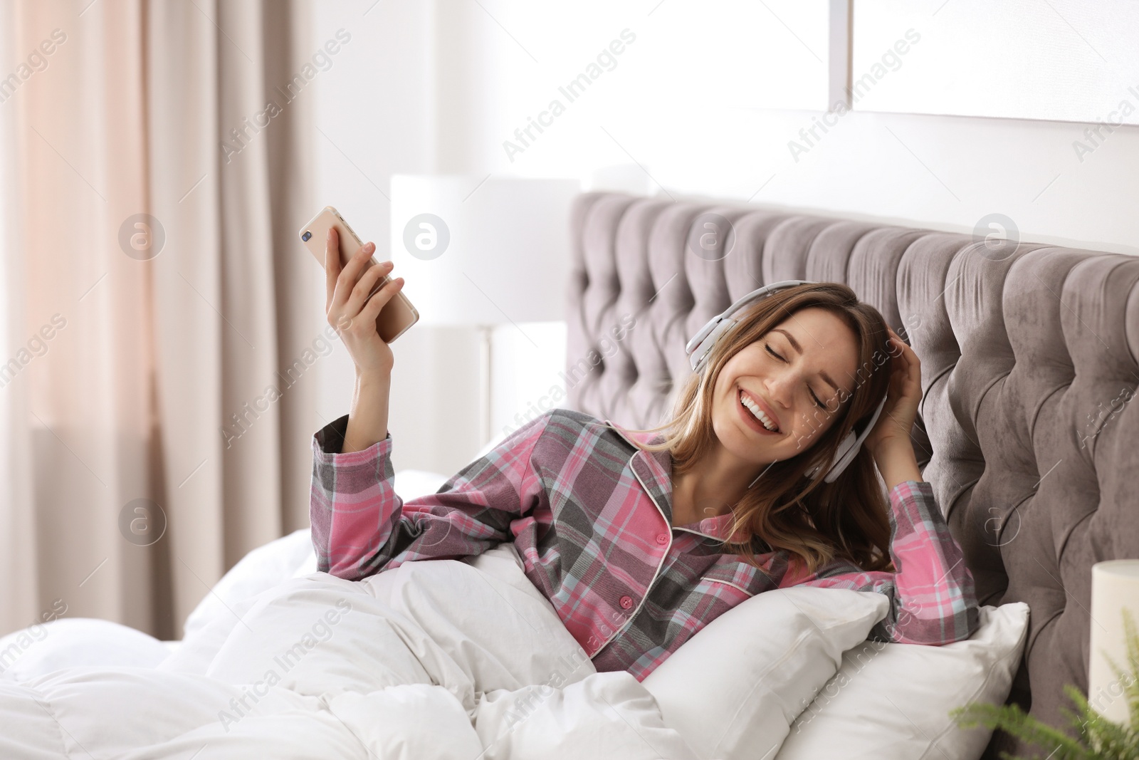 Photo of Young woman with headphones and mobile device enjoying music in bed