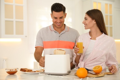 Photo of Happy couple preparing breakfast with toasted bread at table in kitchen