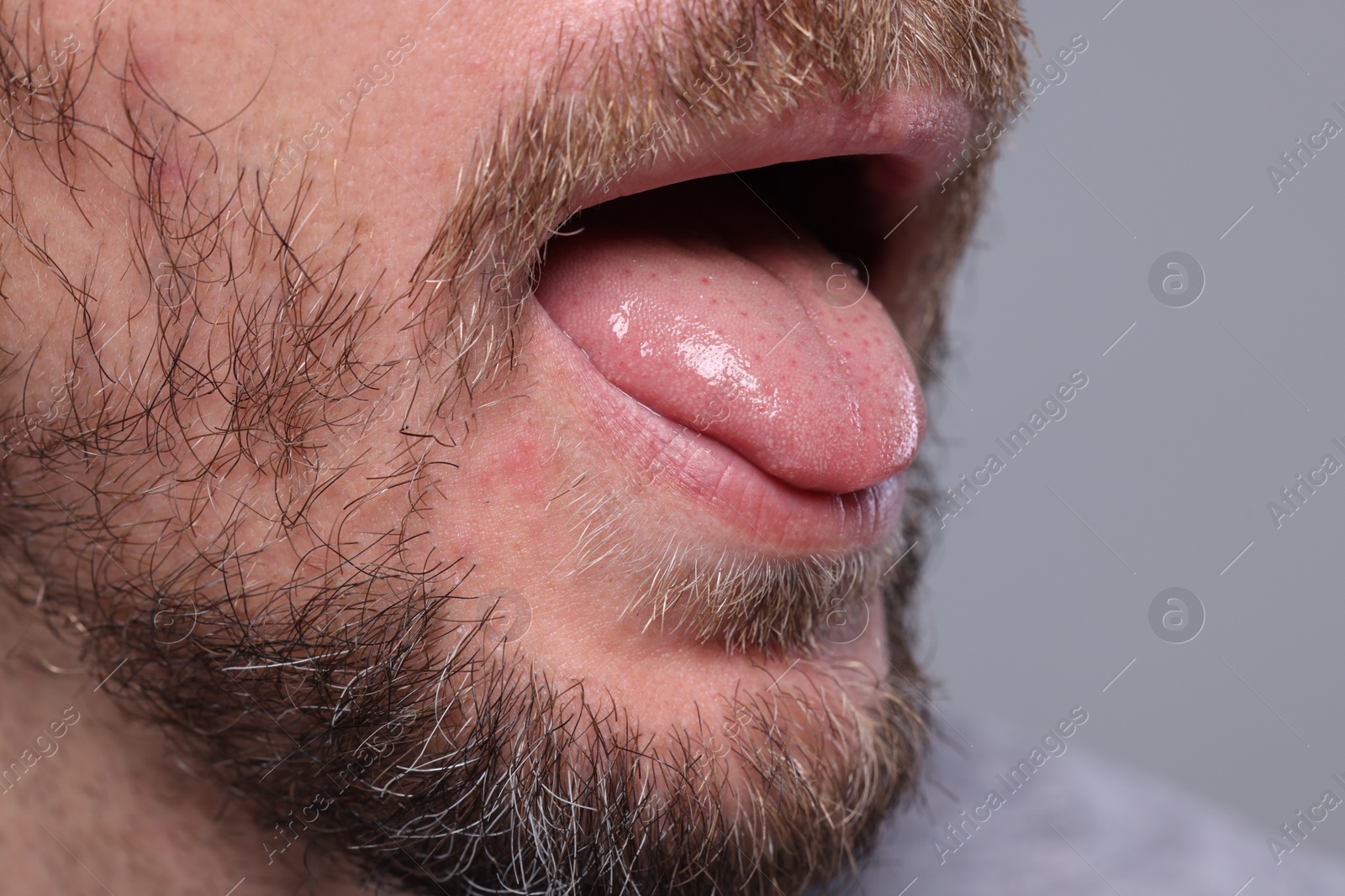 Photo of Closeup view of man showing his tongue on grey background