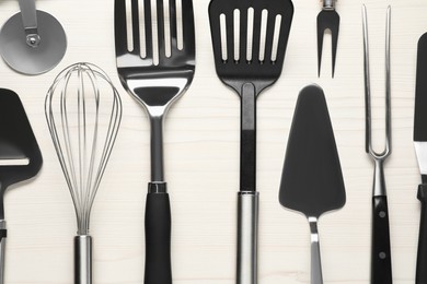 Photo of Different spatulas and other kitchen utensils on light wooden table, flat lay