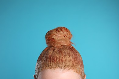 Photo of Young woman dyeing her hair with henna on light blue background, closeup