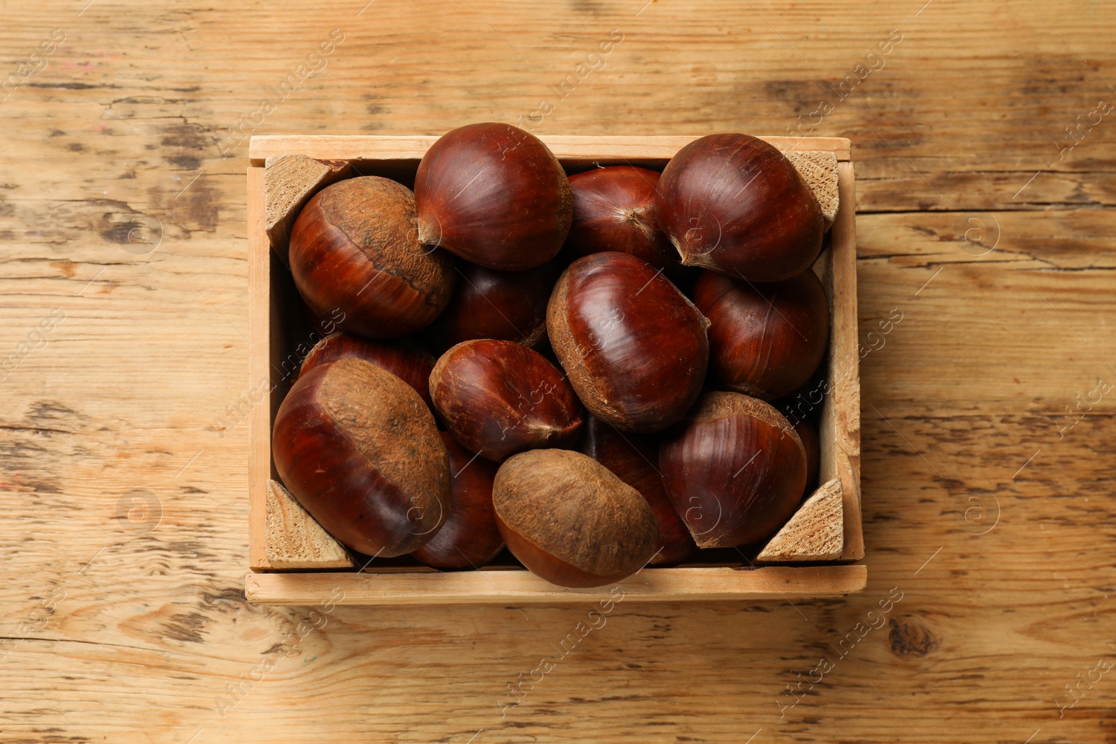 Photo of Sweet fresh edible chestnuts in crate on wooden table, top view