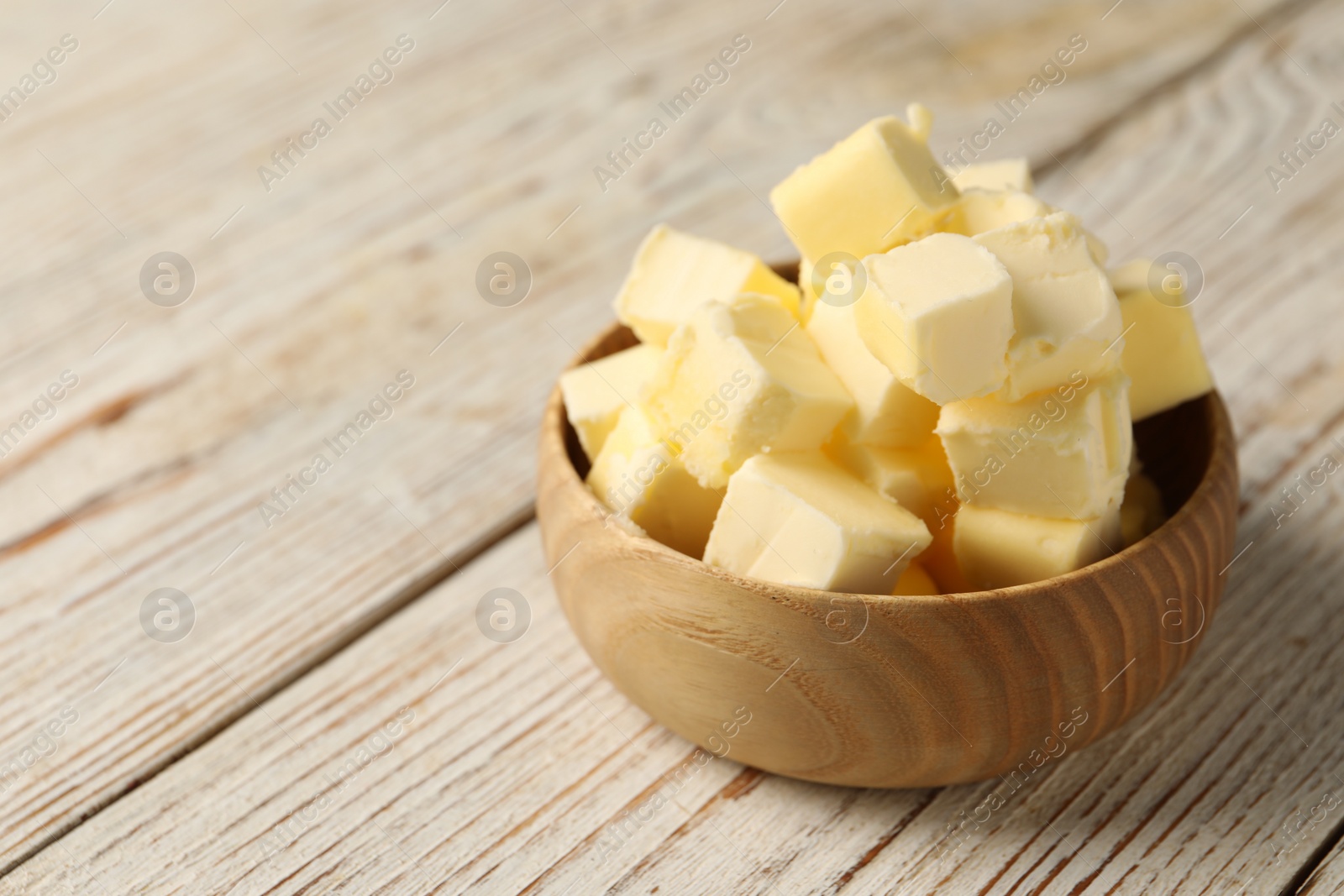 Photo of Tasty butter cubes in bowl on light wooden table. Space for text