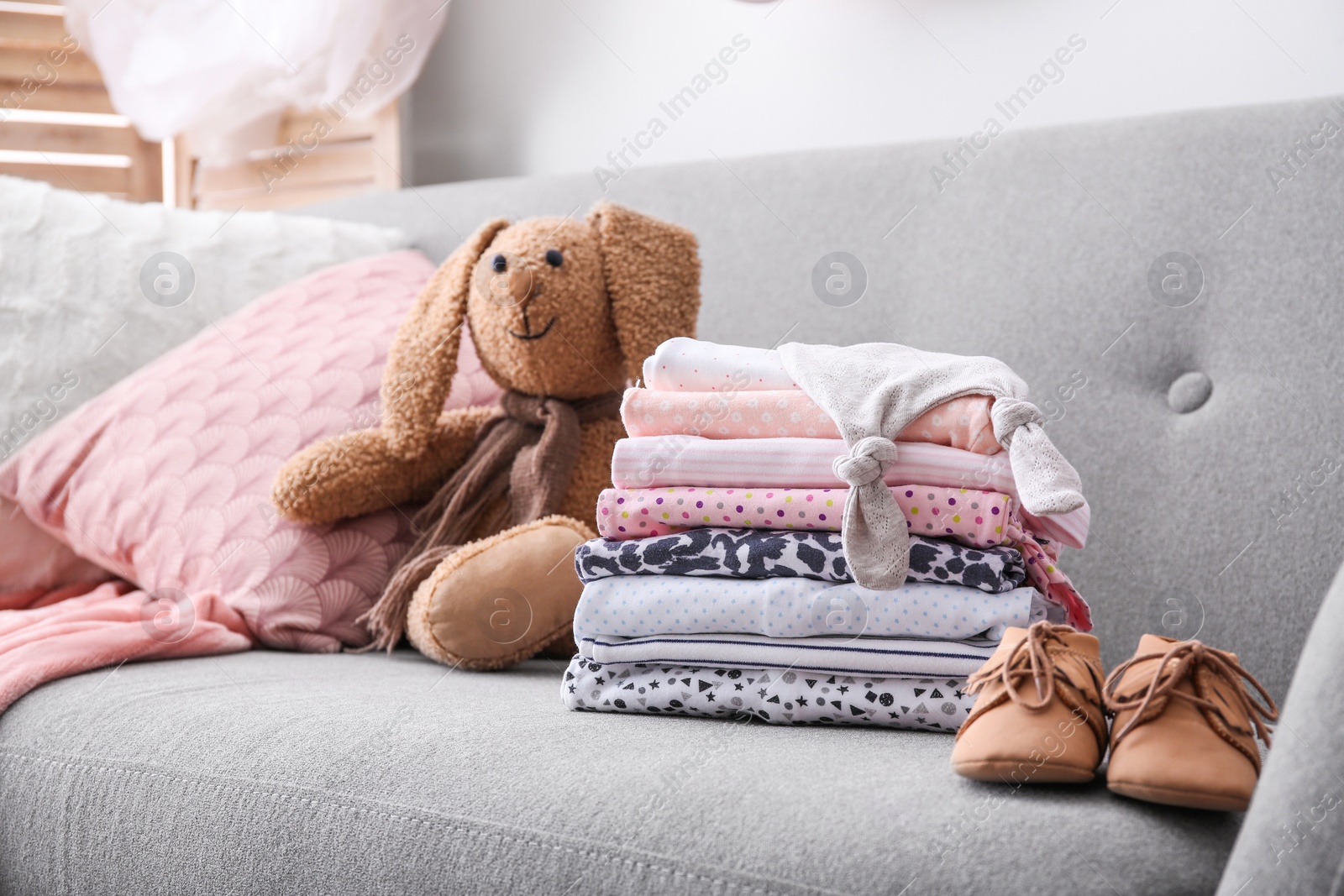 Photo of Stack of stylish child clothes, shoes and toy bunny on couch indoors