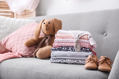 Stack of stylish child clothes, shoes and toy bunny on couch indoors