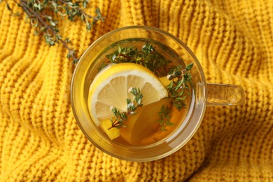 Fresh thyme tea with pieces of lemon on yellow knitted blanket, top view