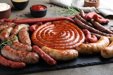 Photo of Different delicious sausages with rosemary and sauces on wooden table, closeup. Assortment of beer snacks