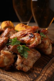 Photo of Delicious baked chicken wings and glasses with beer on wooden table, closeup