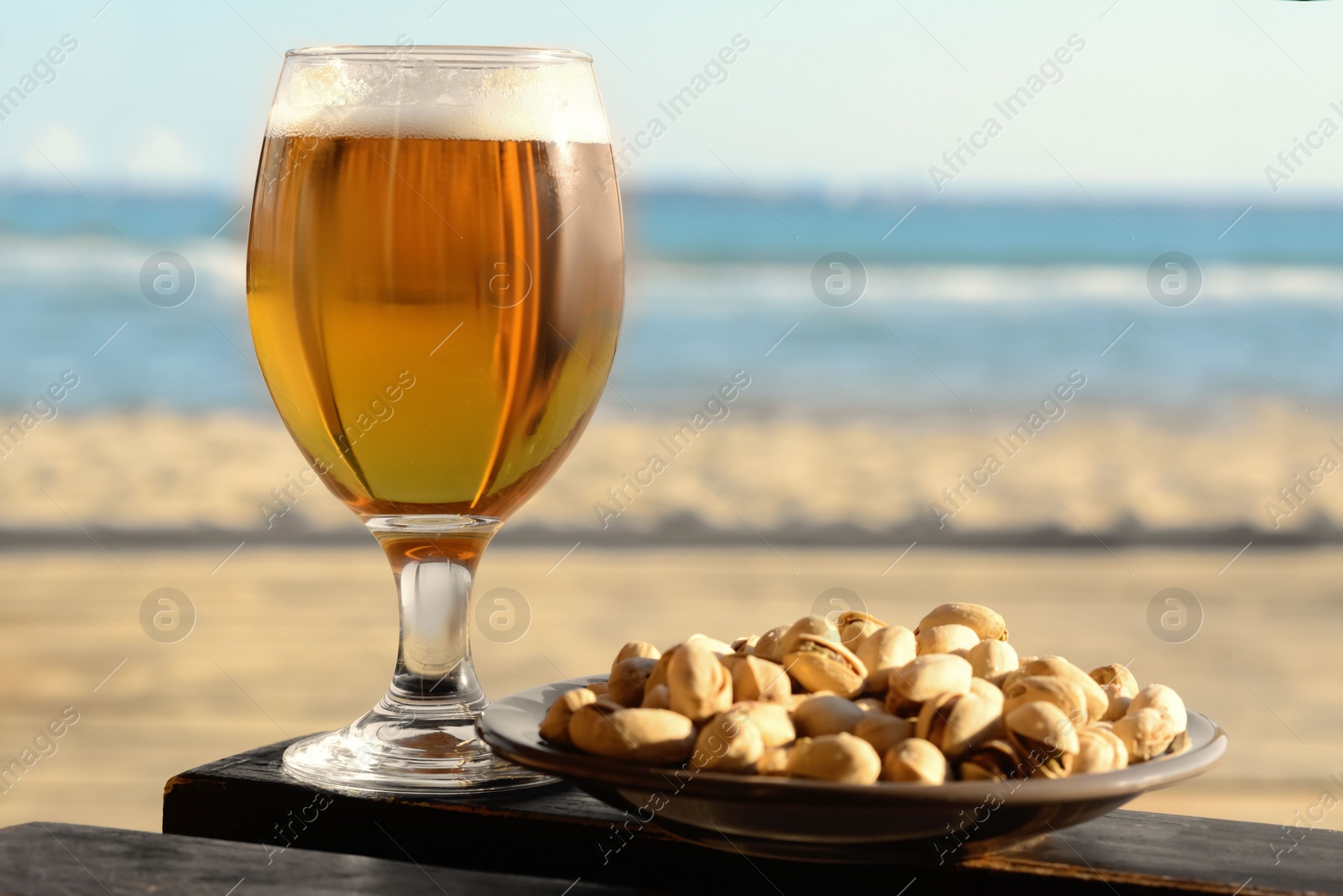 Photo of Glass of cold beer and pistachios on wooden table near sea