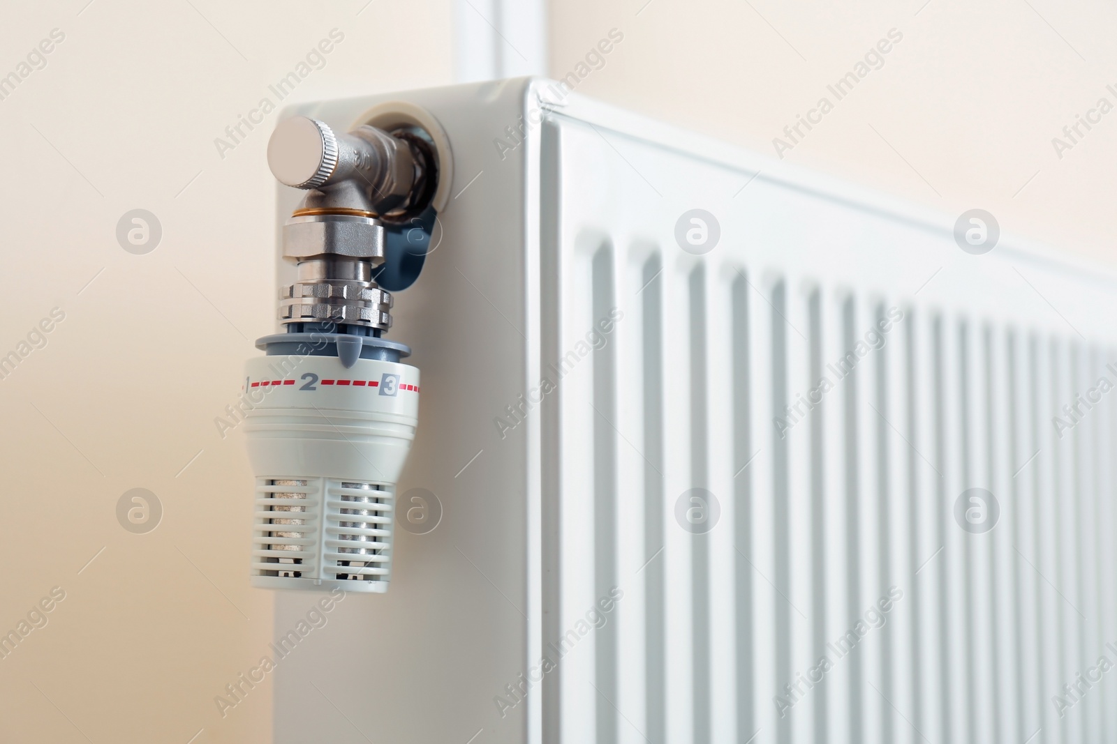 Photo of Heating radiator with thermostat near light wall, closeup