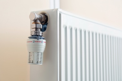 Heating radiator with thermostat near light wall, closeup