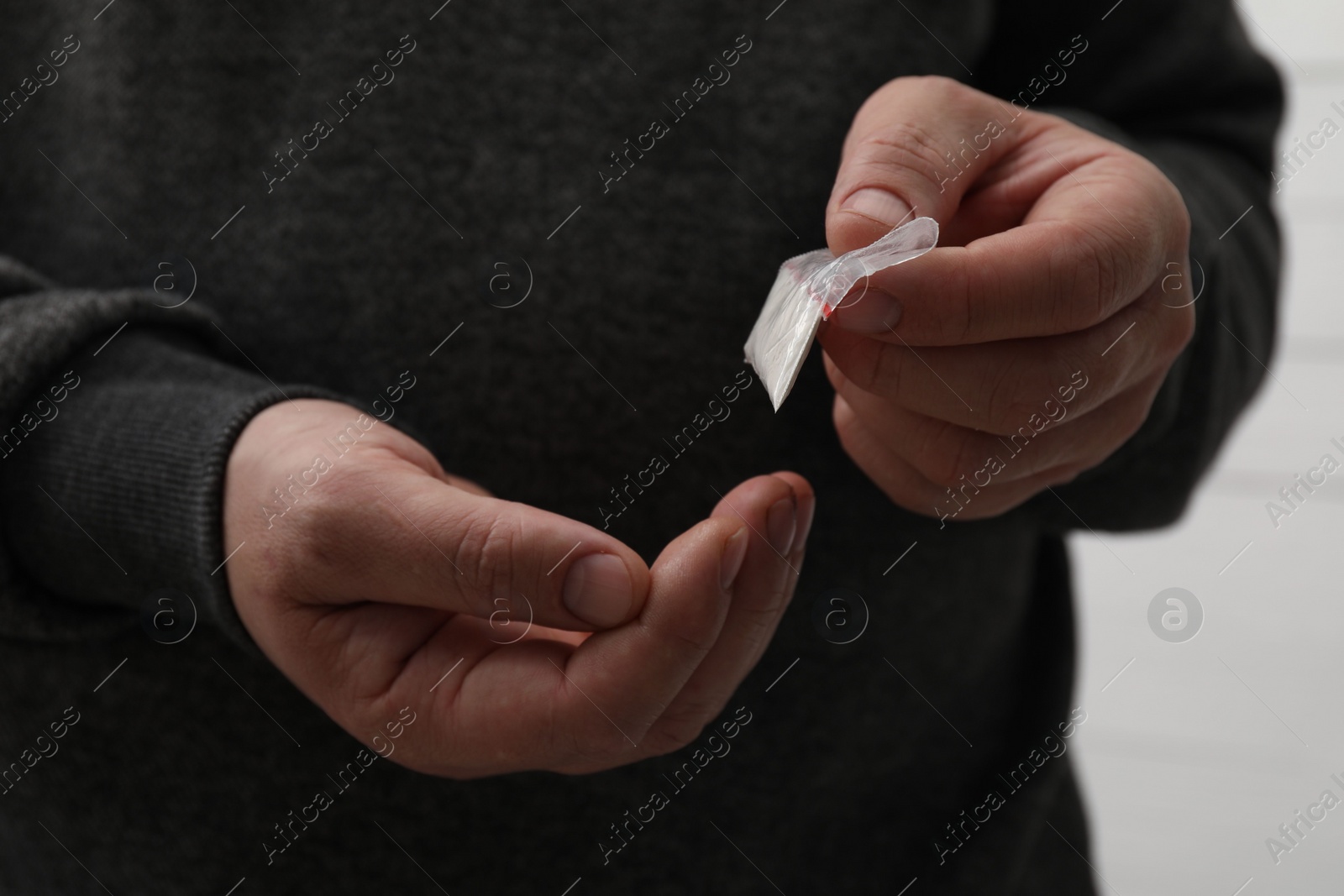 Photo of Drug addiction. Man with plastic bag of cocaine on light background, closeup