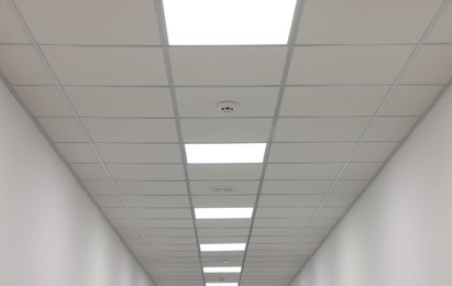 Photo of White ceiling with PVC tiles and lighting indoors, low angle view