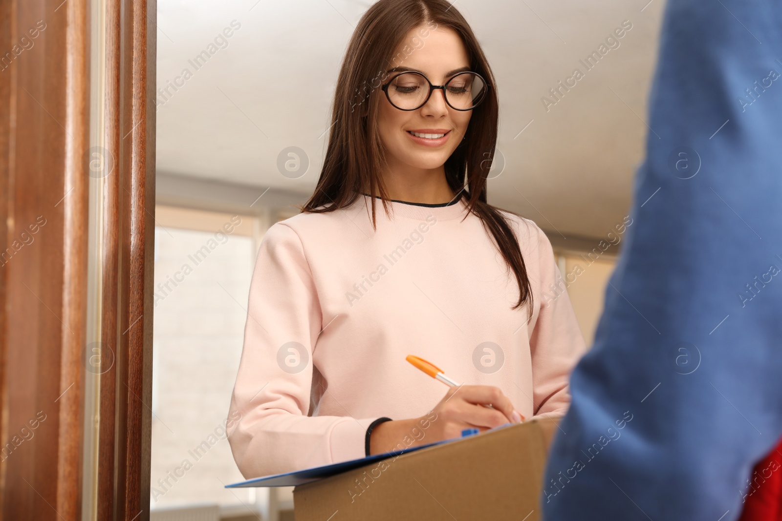 Photo of Woman receiving parcel from delivery service courier indoors