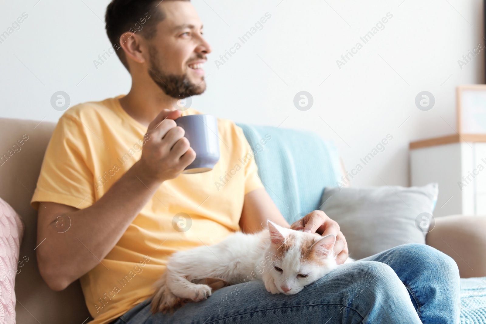 Photo of Young man with cute cat on sofa at home