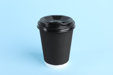 Black paper cup with plastic lid on light blue background. Coffee to go