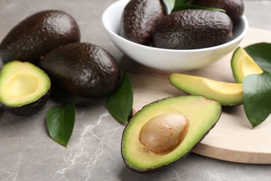 Whole and cut avocados with green leaves on grey marble table