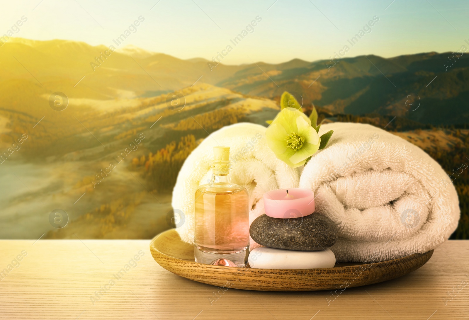 Image of Tray with spa supplies on wooden table against beautiful mountain landscape in morning, space for text