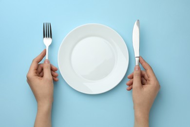 Woman with fork, knife and clean plate at light blue table, top view