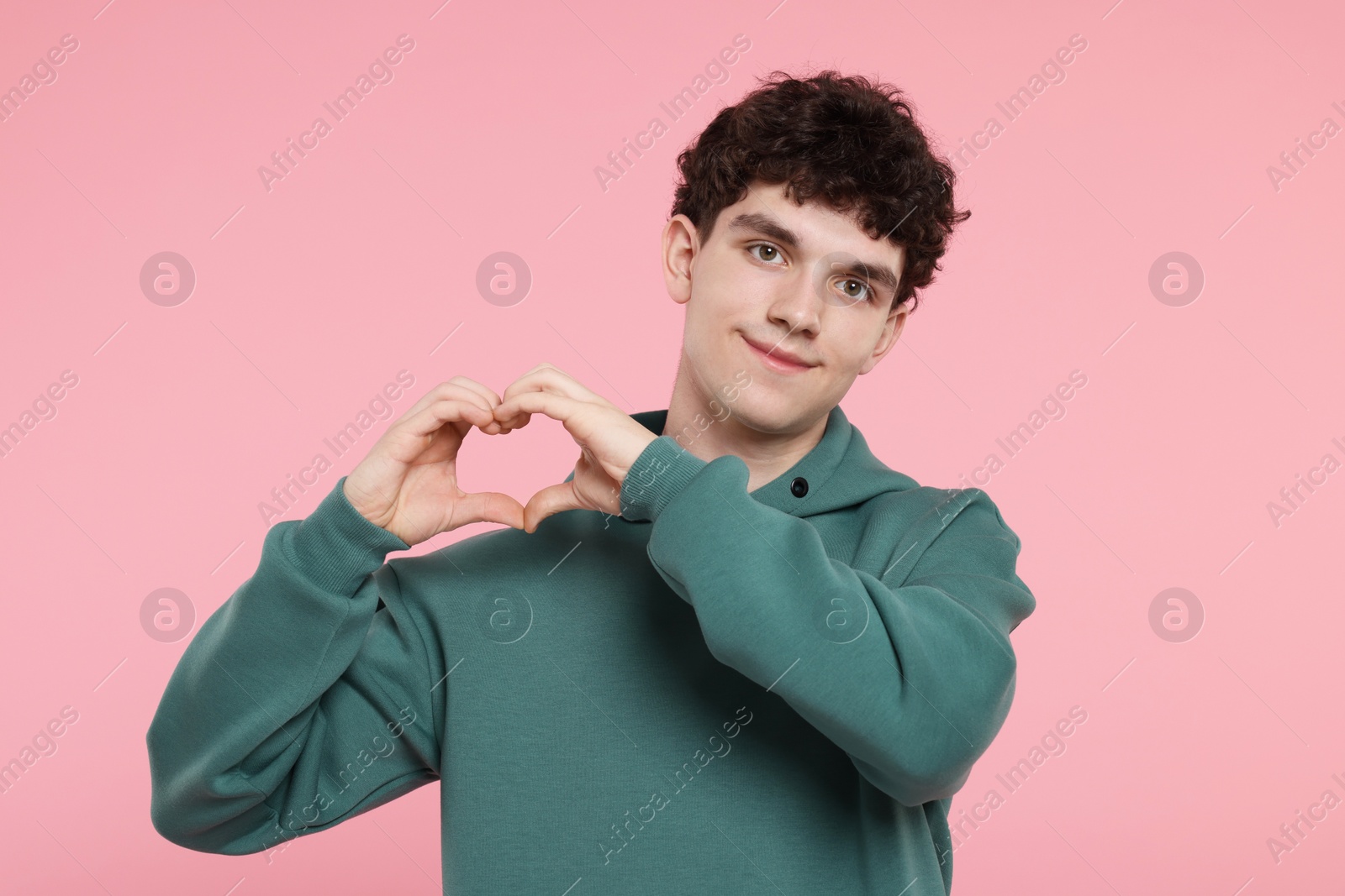 Photo of Happy young man showing heart gesture with hands on pink background