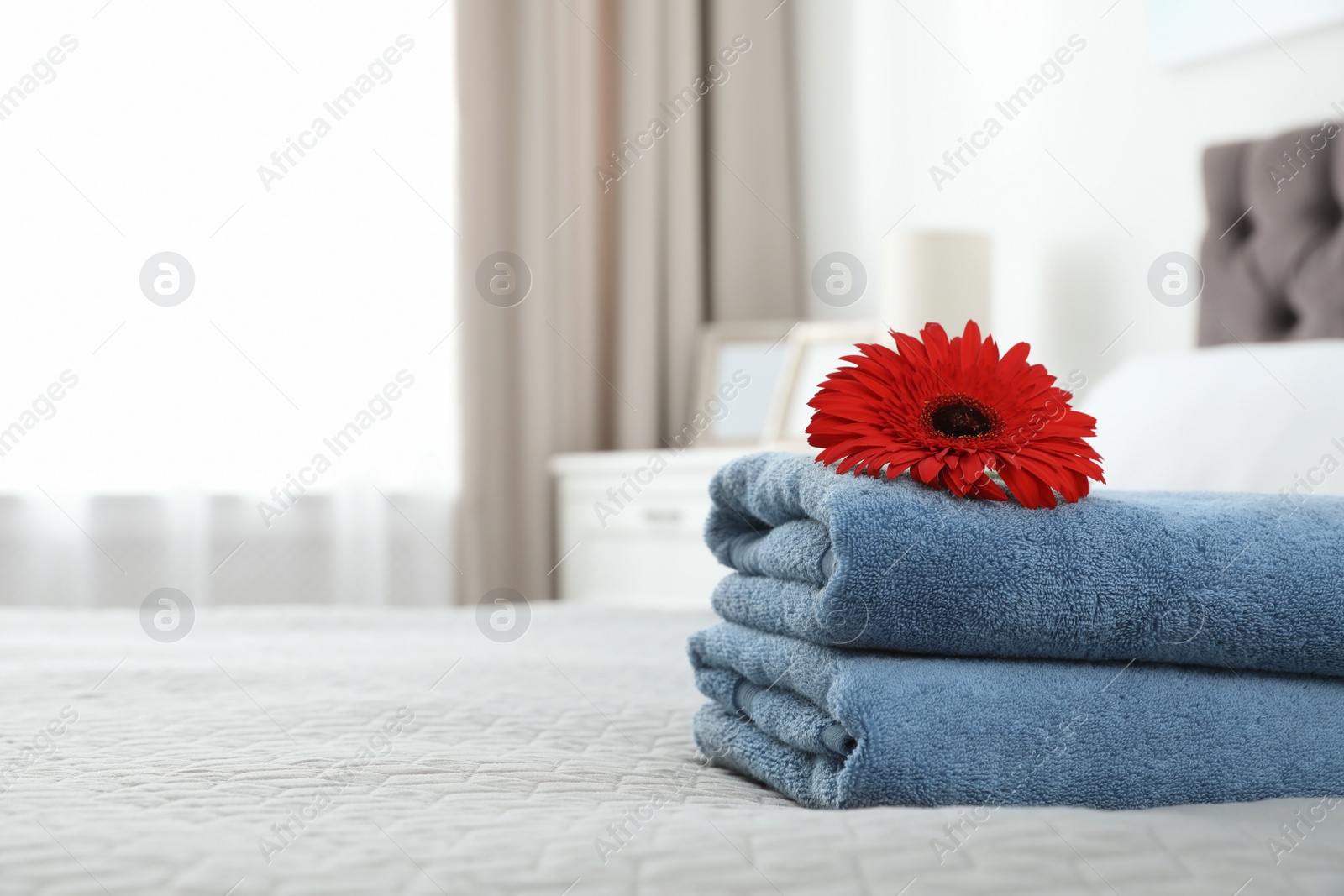 Photo of Stack of clean towels with flower on bed indoors. Space for text