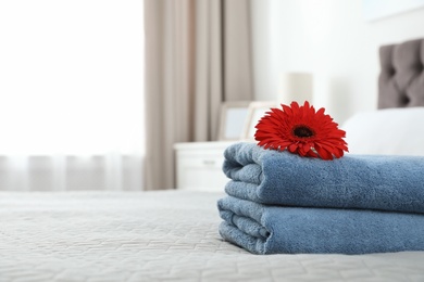 Photo of Stack of clean towels with flower on bed indoors. Space for text