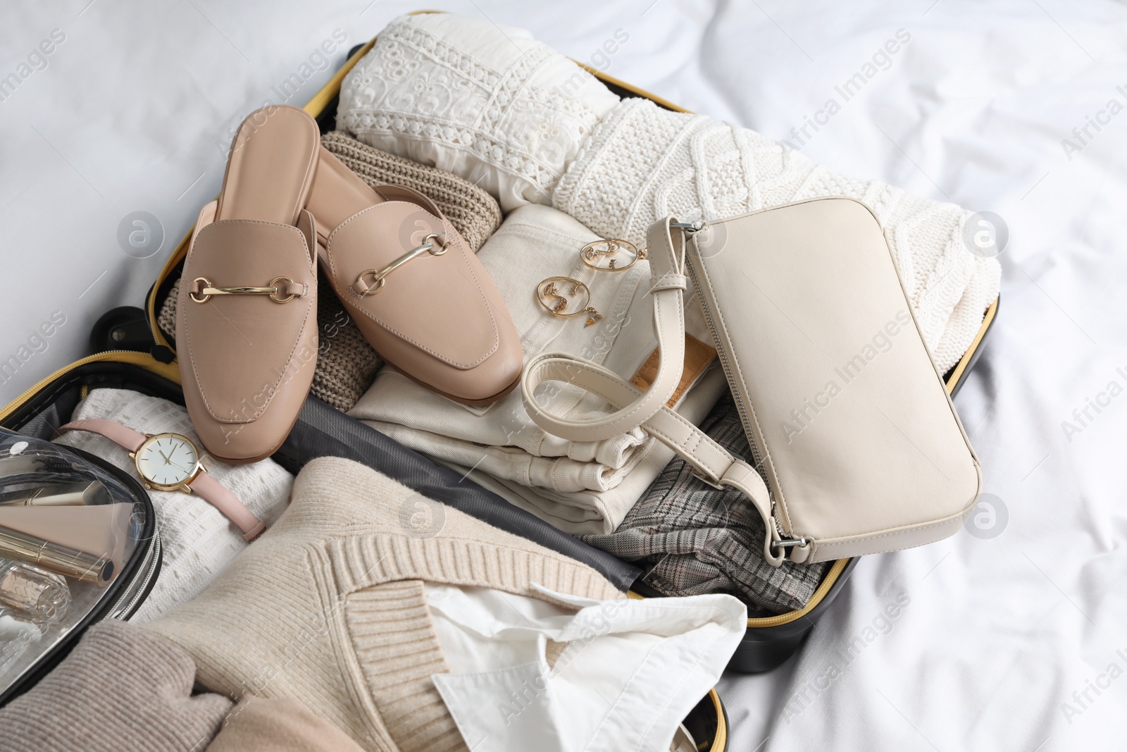 Photo of Open suitcase with folded clothes, shoes and accessories on bed