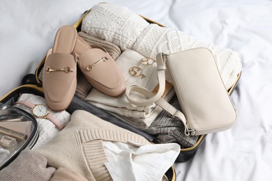 Photo of Open suitcase with folded clothes, shoes and accessories on bed