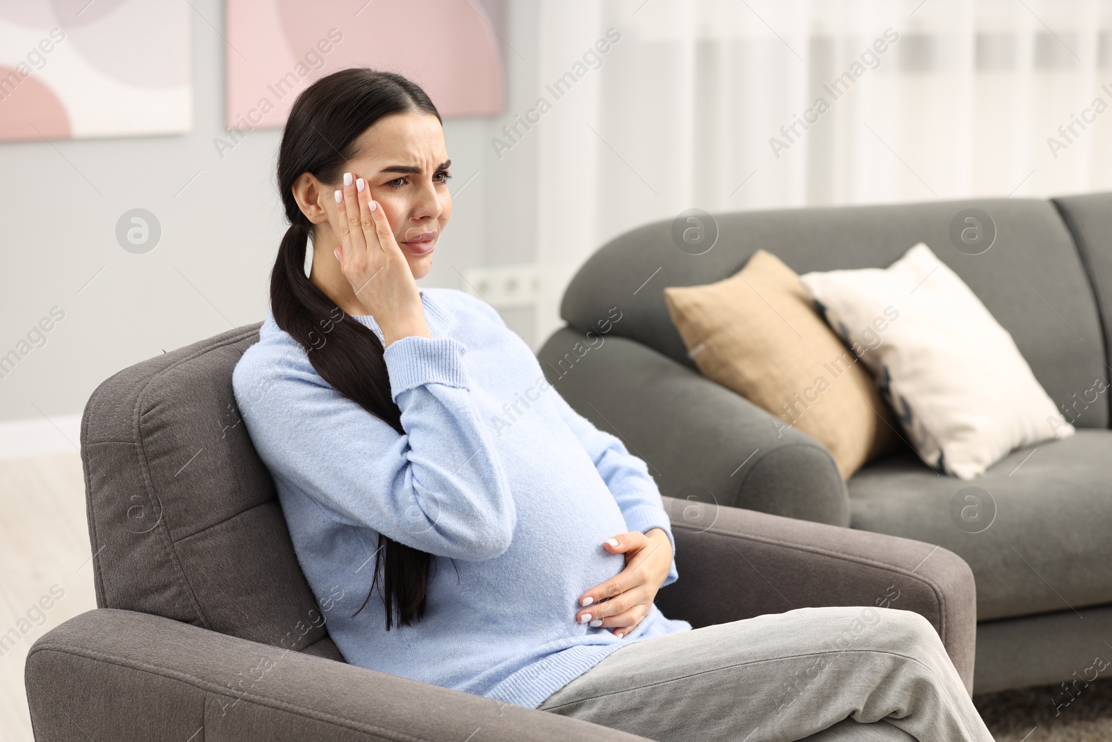 Photo of Pregnant woman suffering from headache on armchair at home