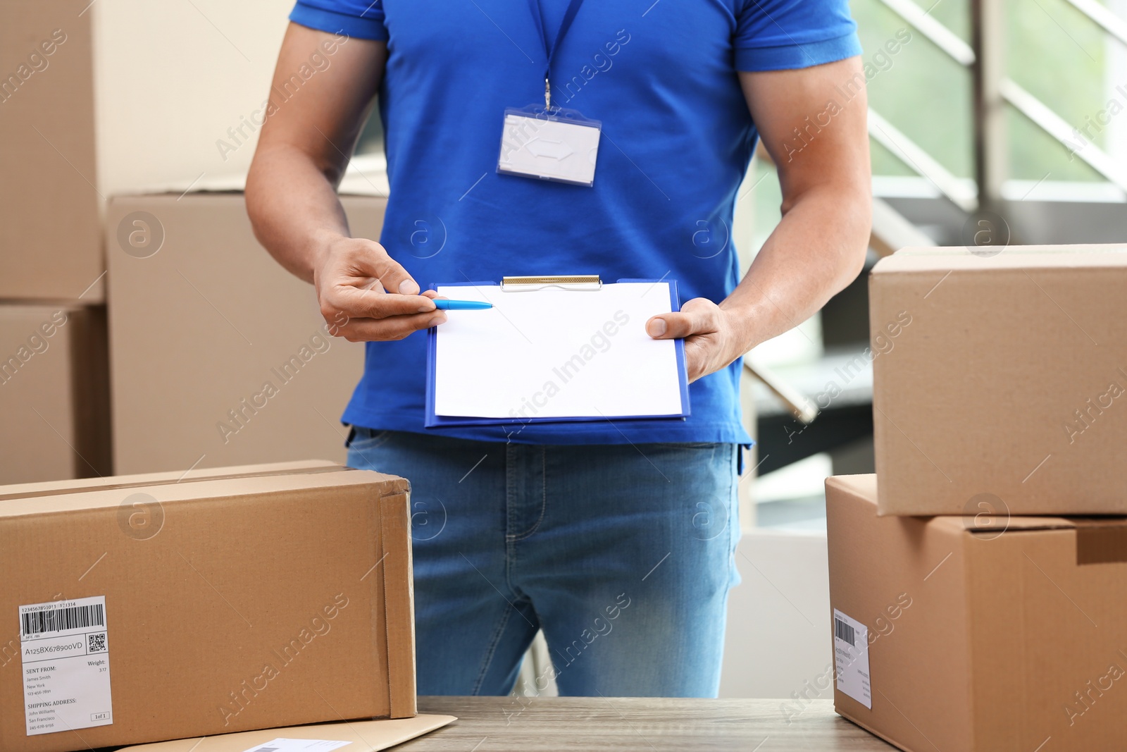 Photo of Young courier with clipboard among parcels at delivery department