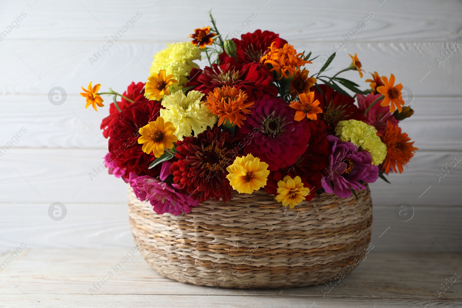 Photo of Beautiful wild flowers in wicker basket on light wooden table