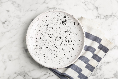 Photo of Empty patterned plate and napkin on white marble table, flat lay