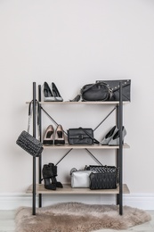 Shelving unit with stylish shoes and purses near white wall. Element of dressing room interior