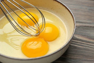 Photo of Whisking eggs in bowl on wooden table, closeup