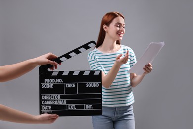 Photo of Actress performing role while second assistant camera holding clapperboard on grey background, selective focus