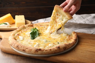 Photo of Woman taking piece of delicious cheese pizza at wooden table, closeup