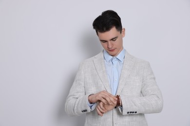 Photo of Handsome young man checking time on his wristwatch against white background, space for text