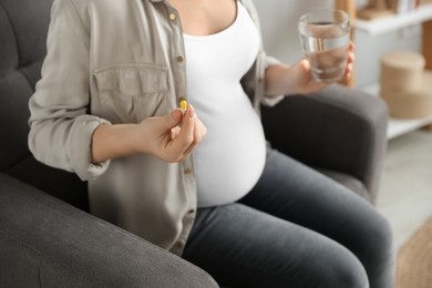 Photo of Pregnant woman holding pill and glass with water indoors, closeup
