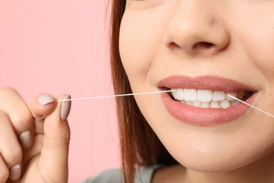 Young woman flossing teeth on color background, closeup