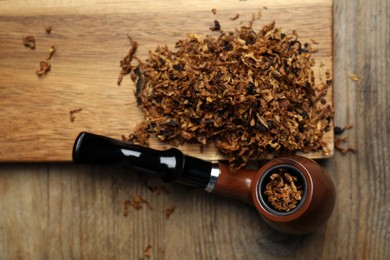 Photo of Smoking pipe and dry tobacco on wooden table, flat lay